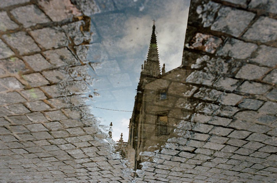 Cobblestone reflection of a historic church tower in a water puddle, captured in Nancy, France.