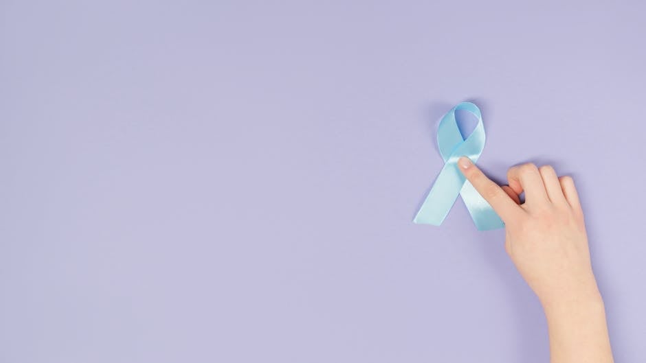 A hand holding a blue awareness ribbon on a light purple background symbolizing support and awareness.